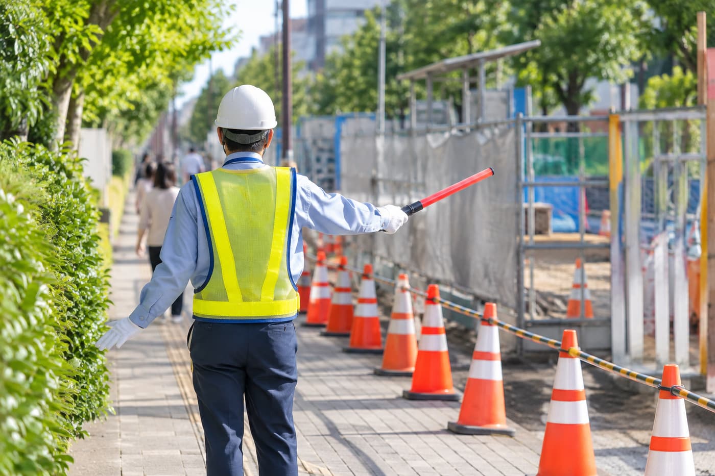 カラーコーンの並ぶ歩道で誘導棒を持つ交通誘導警備員